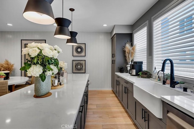 kitchen featuring sink, light hardwood / wood-style flooring, dishwasher, hanging light fixtures, and wood walls