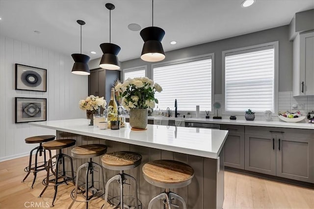 kitchen featuring decorative light fixtures, gray cabinetry, a kitchen breakfast bar, a center island, and light hardwood / wood-style flooring