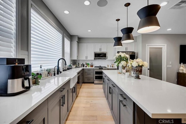 kitchen featuring sink, white cabinetry, pendant lighting, stainless steel appliances, and backsplash