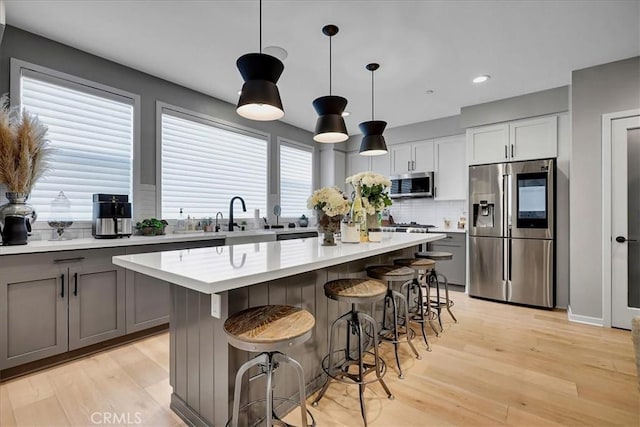 kitchen with a kitchen island, decorative backsplash, hanging light fixtures, stainless steel appliances, and light wood-type flooring