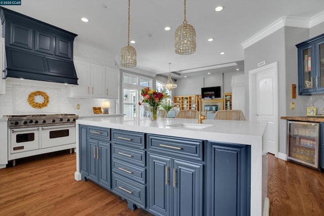 kitchen featuring tasteful backsplash, decorative light fixtures, an island with sink, beverage cooler, and range with two ovens