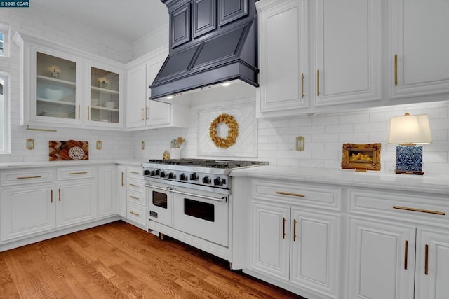 kitchen with range with two ovens, white cabinetry, light hardwood / wood-style floors, backsplash, and custom range hood