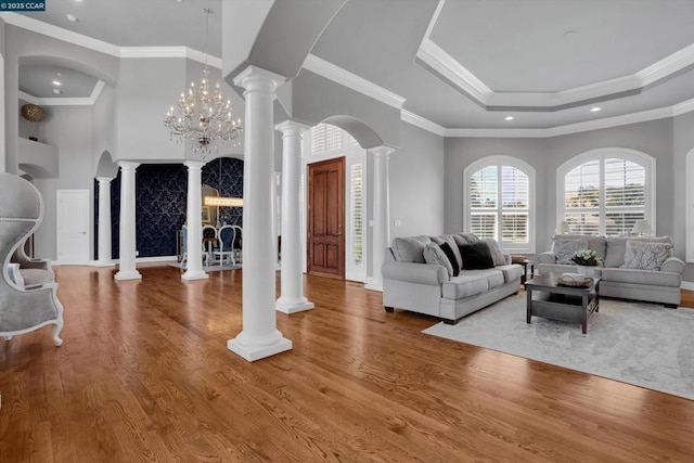 living room with wood-type flooring, crown molding, a raised ceiling, and ornate columns