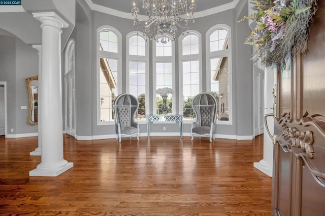 foyer entrance featuring ornamental molding, hardwood / wood-style flooring, a chandelier, and ornate columns