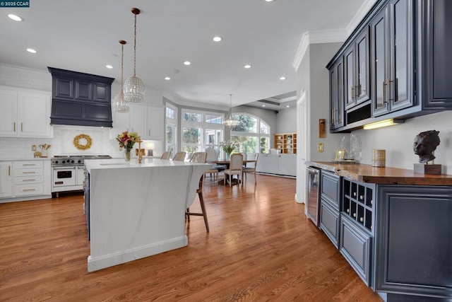 kitchen featuring pendant lighting, a center island, white cabinetry, double oven range, and light hardwood / wood-style flooring