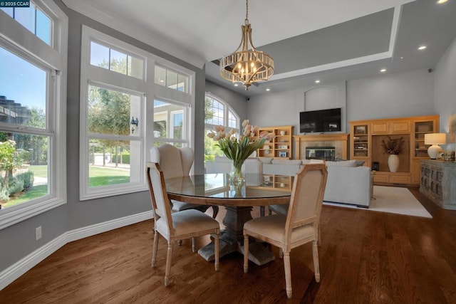 dining room featuring a fireplace, hardwood / wood-style floors, a chandelier, and a high ceiling