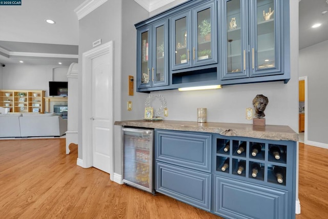 bar with blue cabinets, light hardwood / wood-style floors, ornamental molding, and beverage cooler