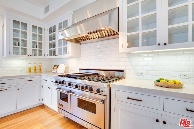 kitchen featuring range with two ovens, white cabinetry, decorative backsplash, ventilation hood, and light stone counters