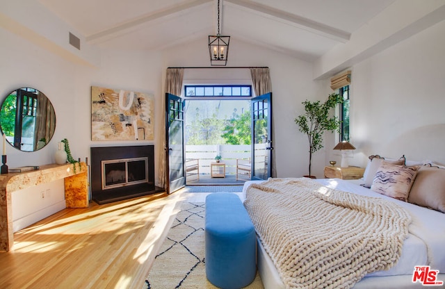 bedroom with wood-type flooring, a fireplace, access to outside, lofted ceiling with beams, and a chandelier