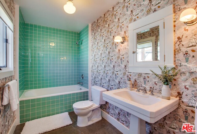 bathroom with tiled shower / bath combo, plenty of natural light, toilet, and tile patterned flooring