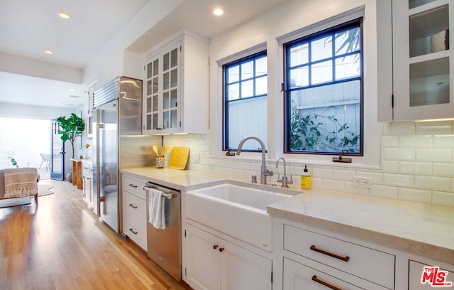 kitchen with white cabinetry, stainless steel appliances, sink, backsplash, and light stone counters