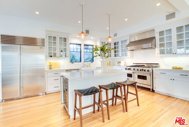 kitchen featuring premium appliances, decorative light fixtures, white cabinetry, wall chimney range hood, and a kitchen island