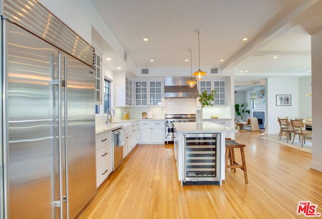 kitchen featuring hanging light fixtures, high quality appliances, wall chimney exhaust hood, white cabinetry, and beverage cooler