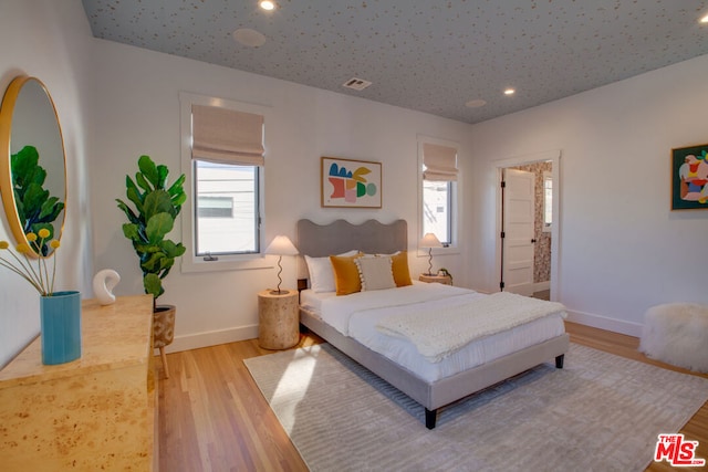 bedroom featuring light wood-type flooring, multiple windows, and ensuite bathroom