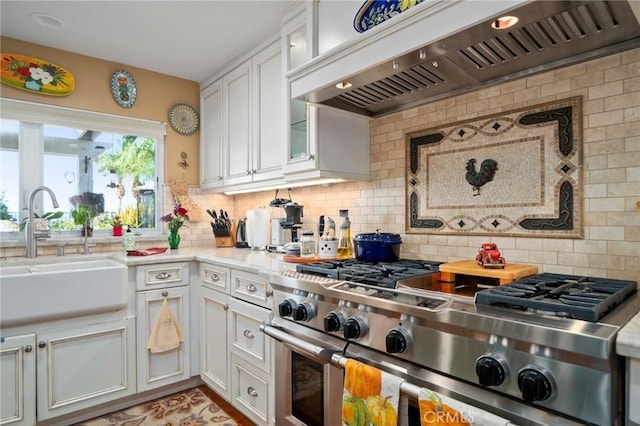 kitchen featuring wall chimney range hood, sink, white cabinetry, backsplash, and range with two ovens