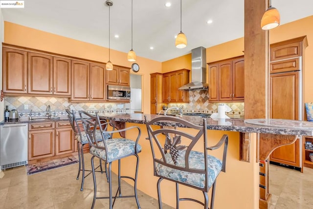 kitchen featuring an island with sink, wall chimney exhaust hood, appliances with stainless steel finishes, and a breakfast bar