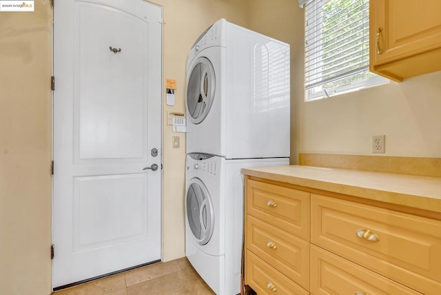 laundry area with light tile patterned floors, cabinets, and stacked washer and clothes dryer