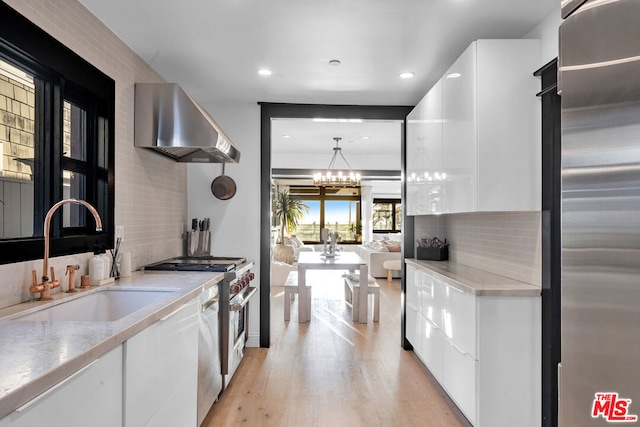 kitchen with sink, hanging light fixtures, appliances with stainless steel finishes, wall chimney range hood, and white cabinets