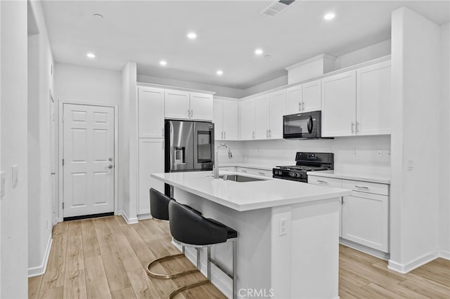 kitchen with black appliances, white cabinetry, a kitchen island with sink, light wood-type flooring, and a breakfast bar