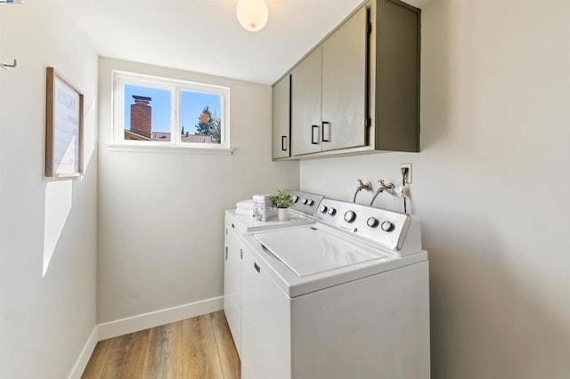 clothes washing area with cabinets, washing machine and dryer, and light wood-type flooring