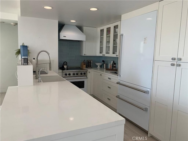 kitchen with tasteful backsplash, sink, white cabinets, stainless steel range, and wall chimney exhaust hood