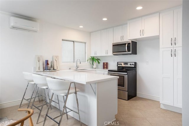 kitchen with an AC wall unit, appliances with stainless steel finishes, white cabinetry, a kitchen breakfast bar, and kitchen peninsula