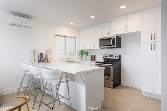 kitchen featuring a kitchen bar, a peninsula, white cabinets, appliances with stainless steel finishes, and an AC wall unit