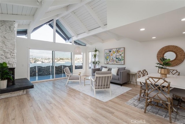 living room featuring a fireplace, light hardwood / wood-style floors, a water view, high vaulted ceiling, and beam ceiling