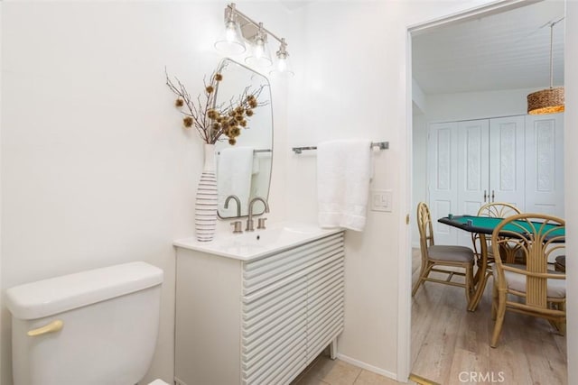 bathroom with toilet, wood finished floors, vanity, and baseboards