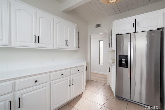 kitchen with visible vents, white cabinets, light tile patterned floors, stainless steel refrigerator with ice dispenser, and beamed ceiling