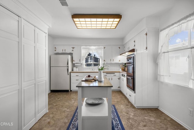 kitchen with white cabinets, a kitchen island, white fridge, decorative backsplash, and multiple ovens