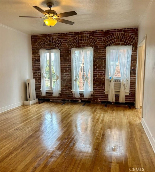 empty room featuring light hardwood / wood-style floors, brick wall, radiator, and ceiling fan