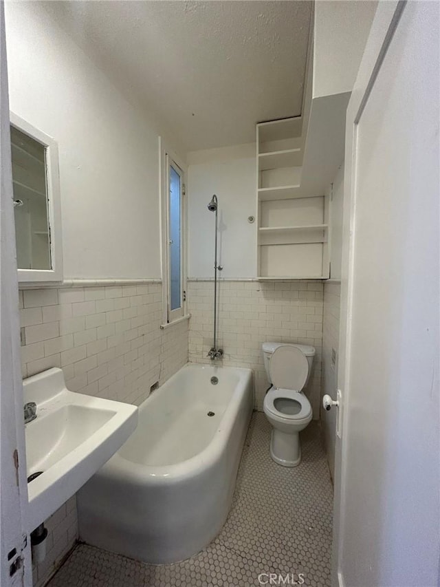 bathroom with tile patterned flooring, sink, tile walls, toilet, and a bath