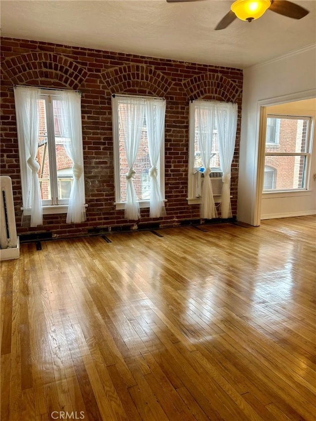 unfurnished room with light wood-type flooring, ceiling fan, and brick wall