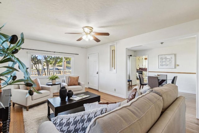 living room with ceiling fan, a textured ceiling, and light wood-type flooring