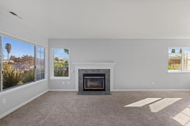 unfurnished living room with plenty of natural light, carpet flooring, and a tiled fireplace