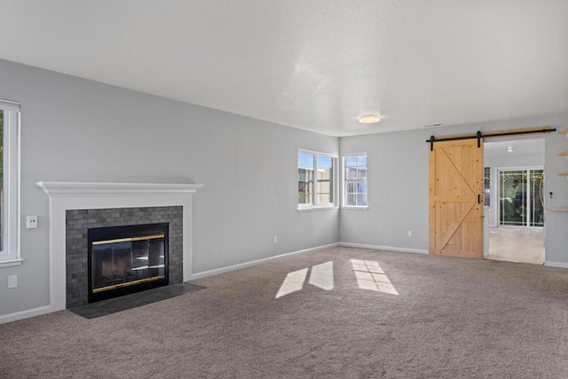 unfurnished living room with a brick fireplace, carpet floors, and a barn door