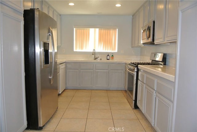 kitchen featuring light tile patterned floors, tile countertops, sink, and appliances with stainless steel finishes