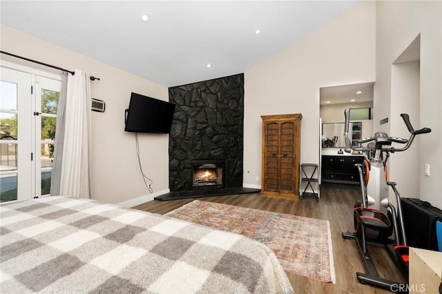 bedroom with access to exterior, a stone fireplace, dark hardwood / wood-style flooring, and lofted ceiling