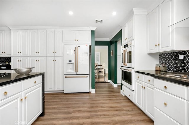 kitchen with white cabinetry, backsplash, white appliances, and light hardwood / wood-style flooring