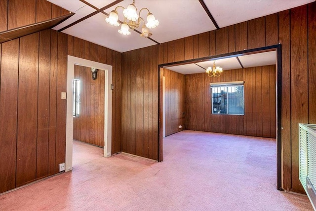 carpeted empty room featuring wooden walls, heating unit, and a notable chandelier