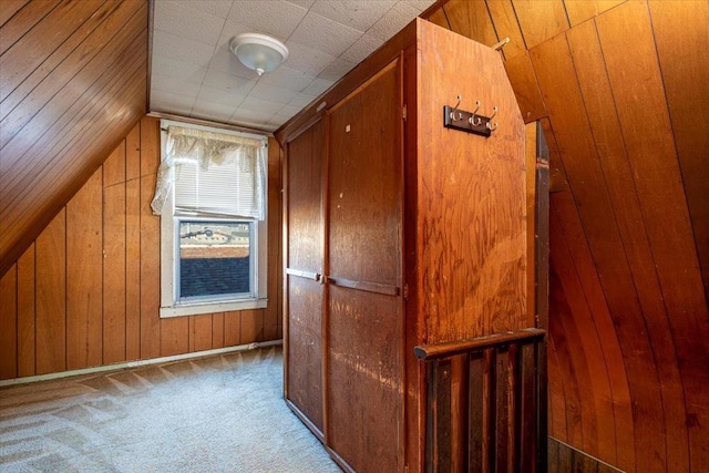 hall with light colored carpet, wooden walls, and lofted ceiling