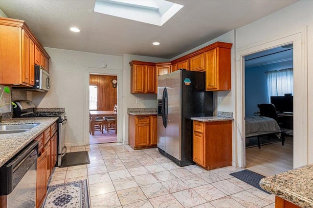 kitchen with sink, stainless steel appliances, a skylight, and light stone counters