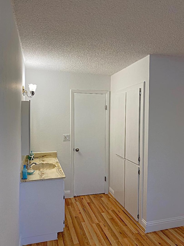 corridor featuring sink, light hardwood / wood-style flooring, and a textured ceiling