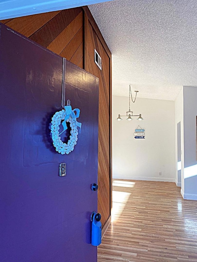 hall featuring a textured ceiling, wood-type flooring, and wooden walls