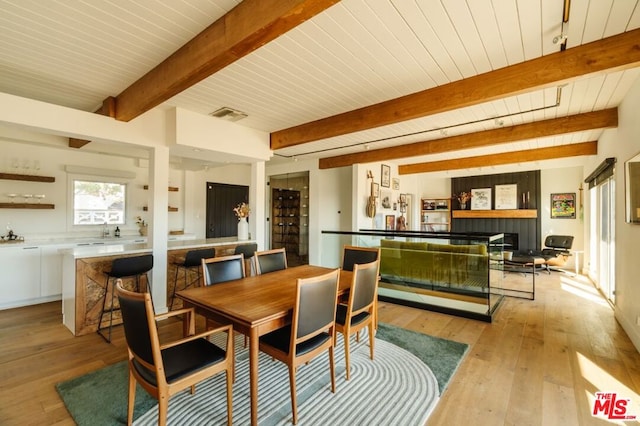 dining room featuring beamed ceiling, wooden ceiling, light wood-type flooring, sink, and a tiled fireplace