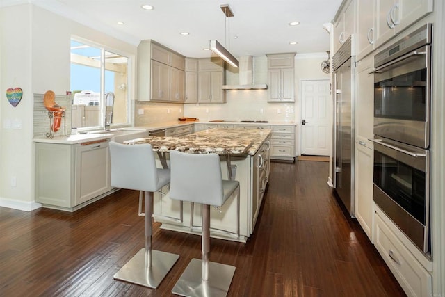 kitchen with appliances with stainless steel finishes, a center island, decorative light fixtures, wall chimney range hood, and sink