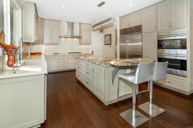 kitchen with a center island, appliances with stainless steel finishes, tasteful backsplash, hanging light fixtures, and wall chimney range hood