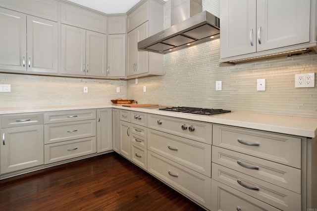 kitchen with dark wood-type flooring, decorative backsplash, wall chimney range hood, and stainless steel gas cooktop