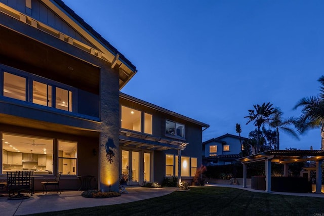 back house at dusk with a patio area, a lawn, and a pergola